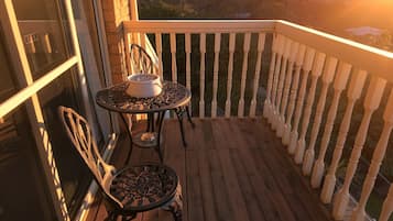 A wooden deck with a white railing, two chairs, and a table with a bowl.