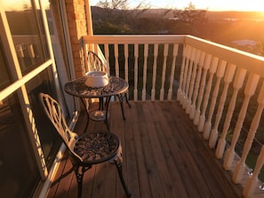 A wooden deck with a white railing, two chairs, and a table with a bowl.
