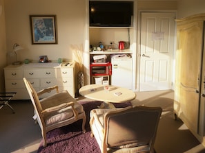 A compact living space with a dining table, two chairs, a television, a kitchenette, and a wardrobe.