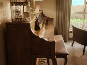 A wooden piano with a bench, a birdcage, and a window with curtains. - Waterview Gardens B&B (Margate)