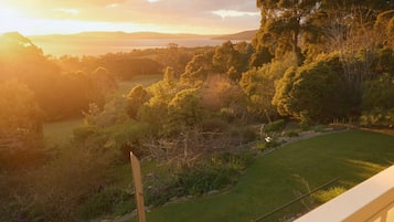 A view of a landscaped garden with a wooden post and a metal water bottle, overlooking a grassy area and trees.