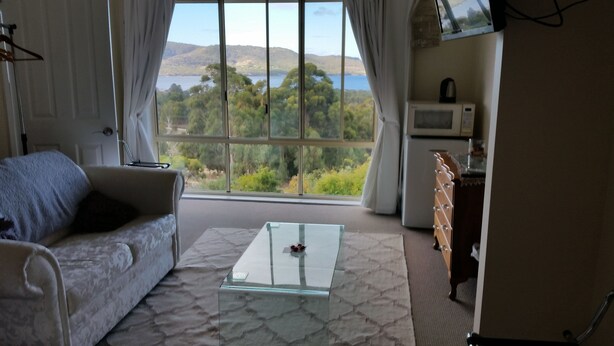 A room with a sofa, a glass coffee table, a view of a lake and hills, and a microwave. - Waterview Gardens B&B (Margate)