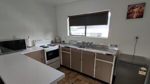 A compact kitchen with white cabinets, a stove, a microwave, a sink, and a refrigerator. - Motel Villa Del Rio (Whangarei)