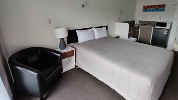 A hotel room with a bed, a chair, a nightstand, a lamp, a microwave, and a refrigerator.