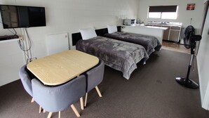 A compact room with a bed, a desk, a chair, a TV, and a fan. - Motel Villa Del Rio (Whangarei)