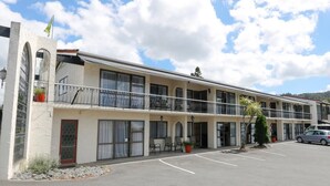 A two-story motel with a balcony on the second floor, a parking lot, and a mountain backdrop. - Motel Villa Del Rio (Whangarei)