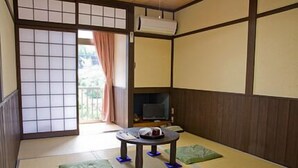A traditional Japanese room with tatami flooring, a tatami mat table, a television, and a sliding door leading to an outdoor area.