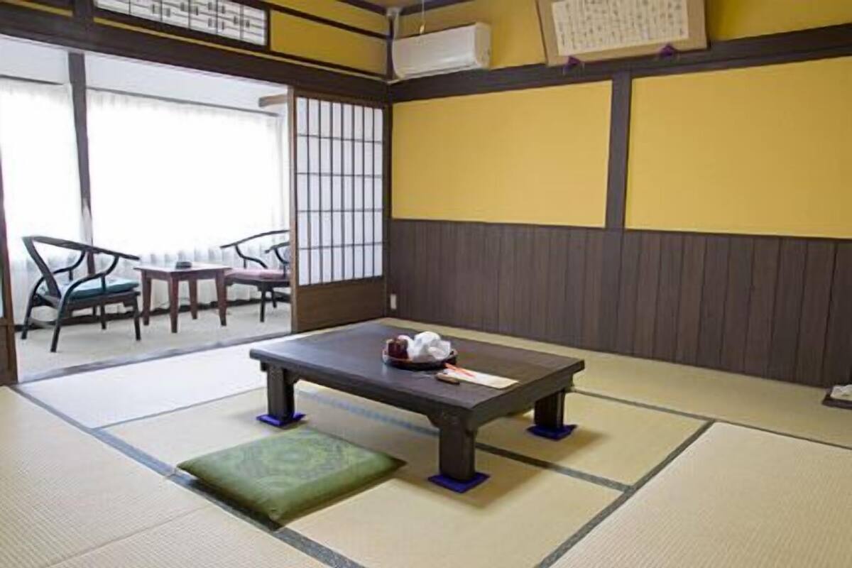 Une pièce avec un sol recouvert de tatamis, une petite table basse, un coussin et une chaise.