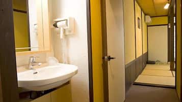 A narrow hallway with a white sink and mirror, a door with a towel dispenser, and a tiled floor.