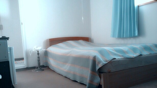 Een slaapkamer met een bed, nachtkastje, lamp en raam met gordijnen.