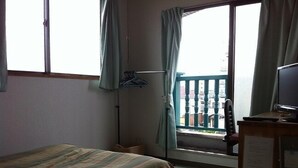 Une chambre d’hôtel avec un lit, un bureau avec un ordinateur, une fenêtre avec des rideaux et une vue sur les bâtiments environnants.