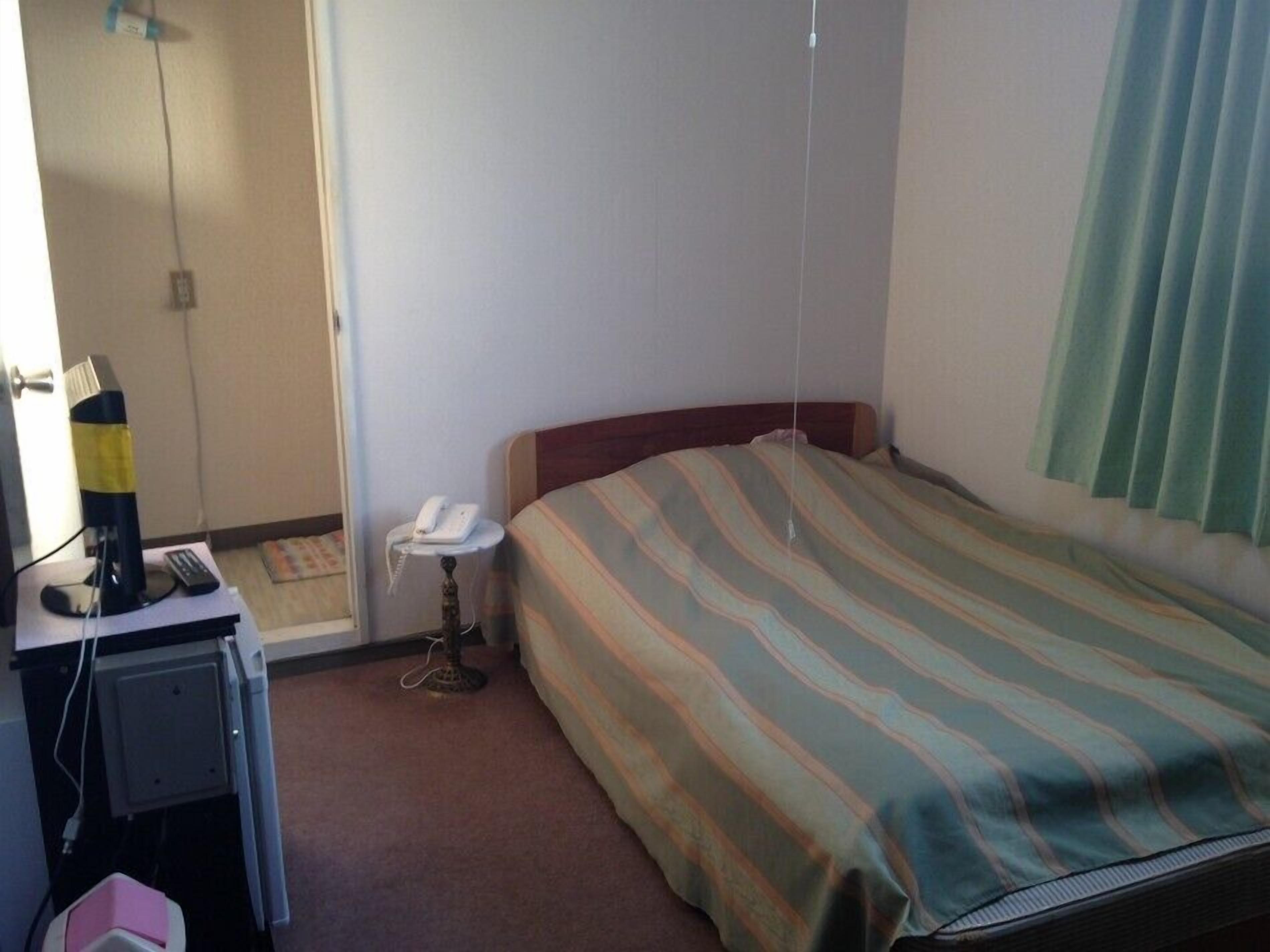 A hotel room with a bed, a desk with a telephone, and a chair.