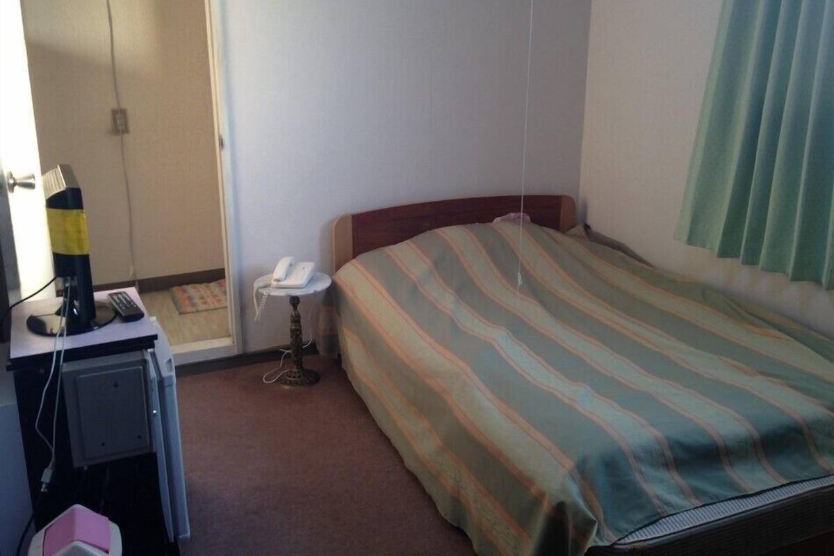 A hotel room with a bed, a desk with a telephone, and a chair.