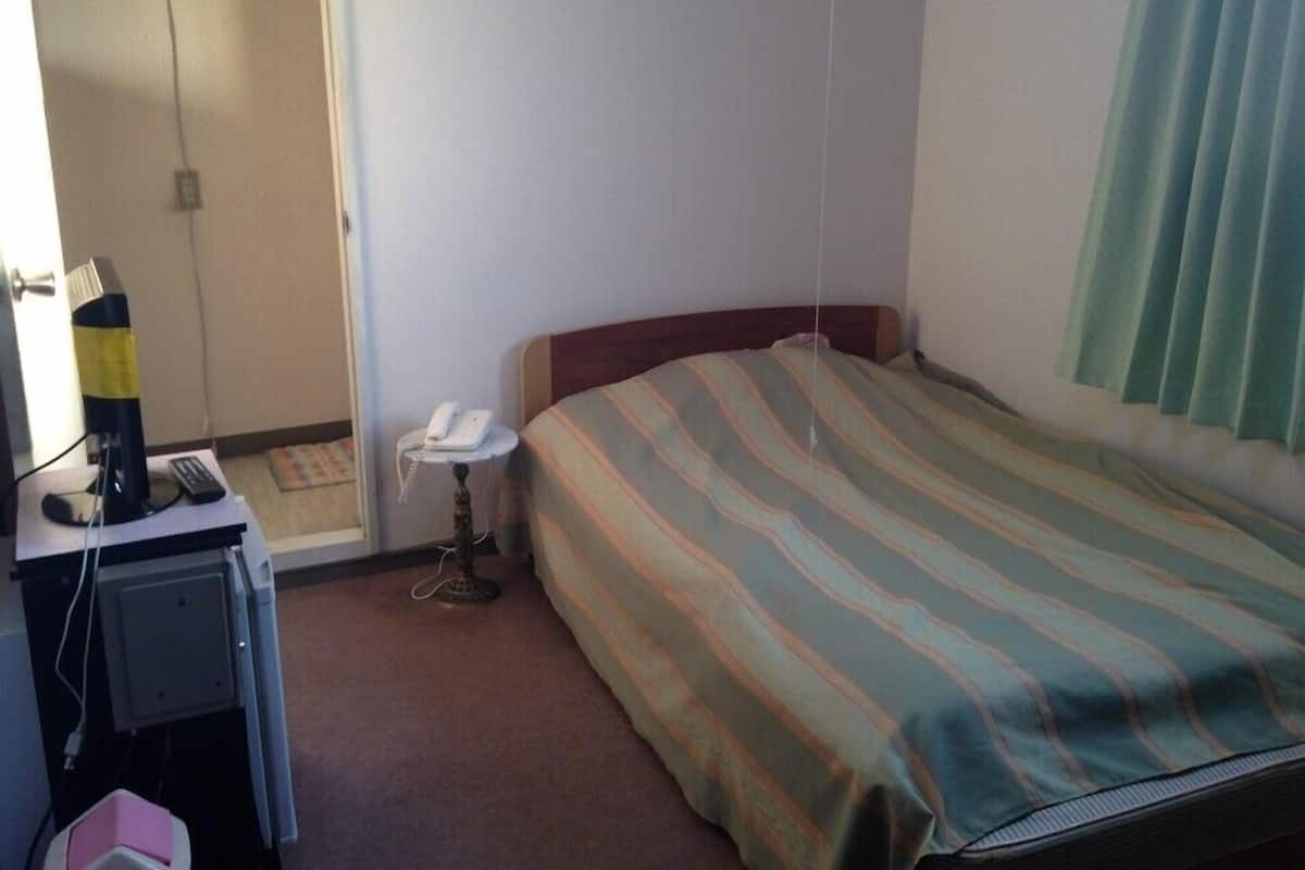 Una habitación de hotel con cama, escritorio, teléfono y una silla.