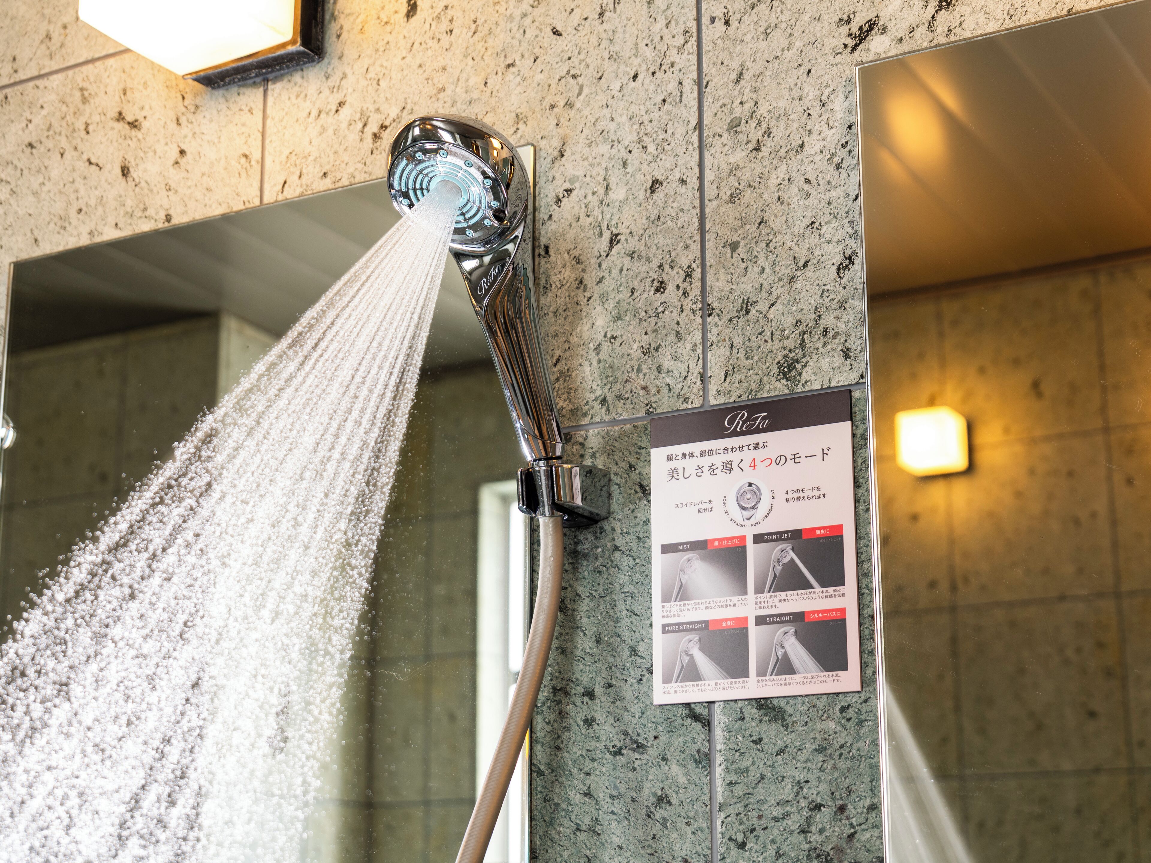 A shower with water spraying down, a sign with Japanese text, and a tiled wall.