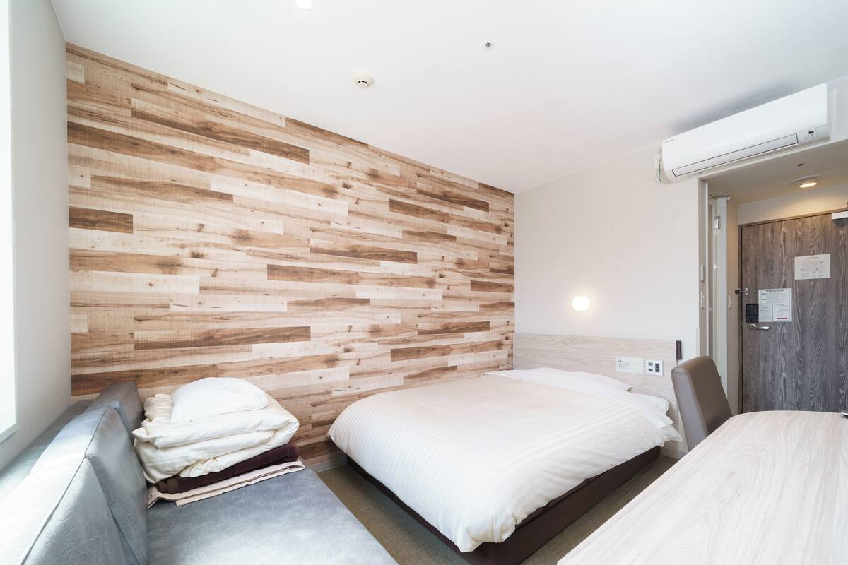 Une chambre d’hôtel moderne avec un mur d’accent en bois, un lit, un coin salon et un bureau.