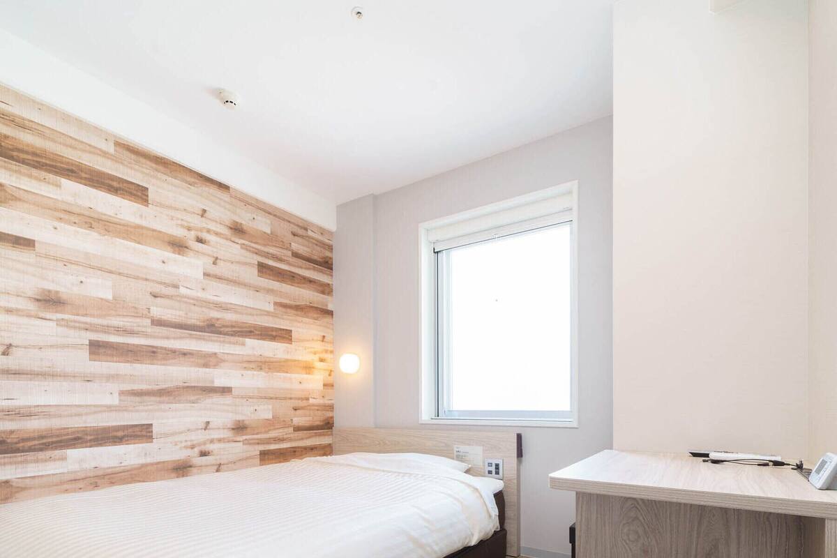 Une chambre à coucher moderne avec une tête de lit en bois, un lit, une table de chevet, une fenêtre et un petit tabouret.