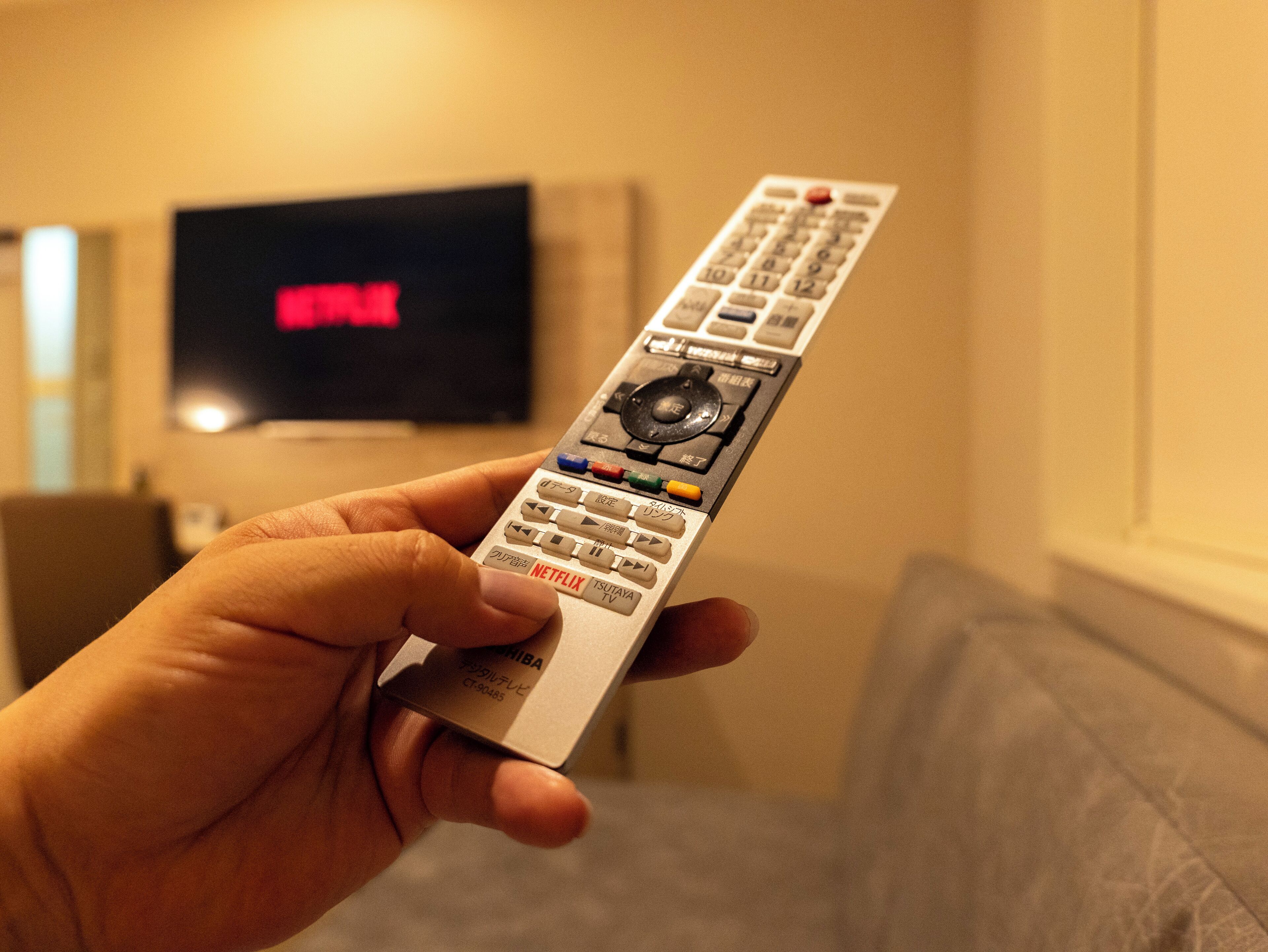 Una mano sosteniendo un control remoto con botones para Netflix, TV y otras funciones.