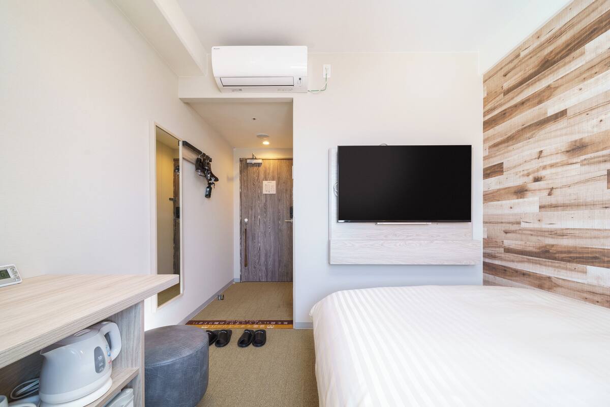 Une chambre d’hôtel moderne dotée d’un grand lit, d’un téléviseur à écran plat fixé au mur, d’une petite kitchenette avec une bouilloire et d’un mur décoratif en bois.