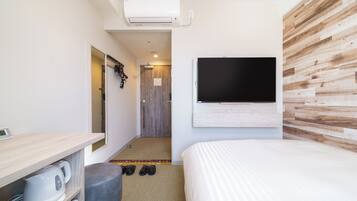 A modern hotel room with a large bed, a flat-screen TV mounted on the wall, a small kitchenette with a kettle, and a wooden accent wall.