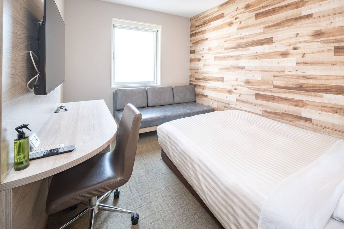 Une chambre d’hôtel avec un mur en bois, un lit, un bureau avec une chaise et une fenêtre.