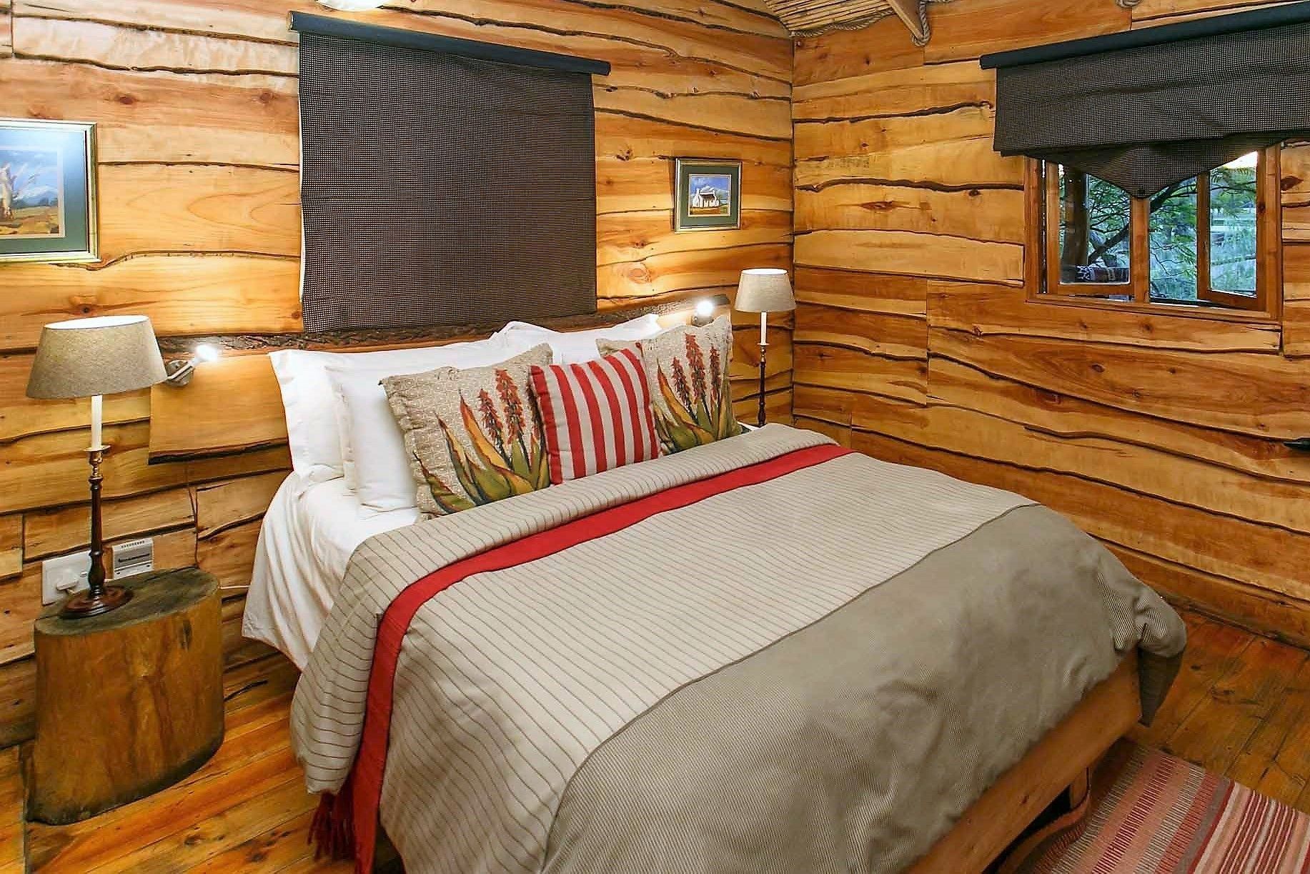 A log cabin bedroom with a bed, two nightstands, a window with a view, and a door.