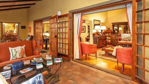 A cozy living room with a sofa, armchairs, a coffee table, and a bookshelf. - Riverside Lodge (Oudtshoorn)