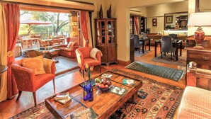 A spacious living area with a sofa, armchairs, a coffee table, and a dining area with chairs and a table. - Riverside Lodge (Oudtshoorn)
