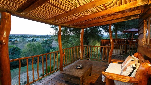 A wooden deck with a bench and a table, overlooking a scenic landscape. - Riverside Lodge (Oudtshoorn)