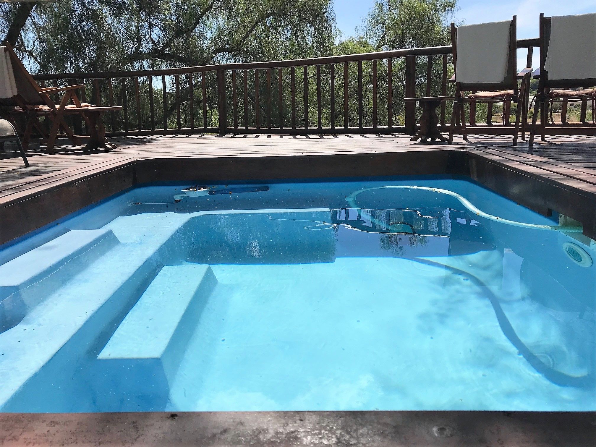 A swimming pool with a wooden deck and chairs around it.