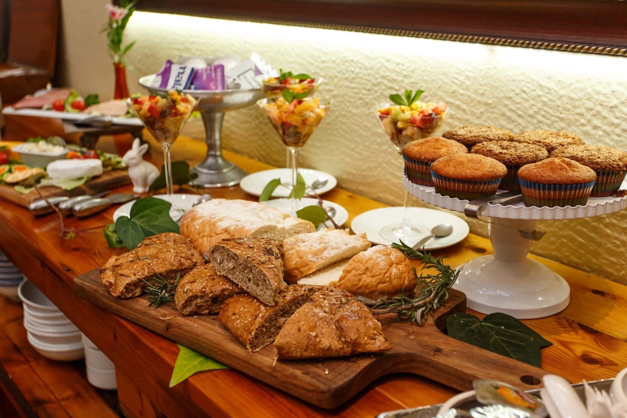 Una mesa de buffet con diferentes opciones de comida, como pan, muffins y copas de fruta.