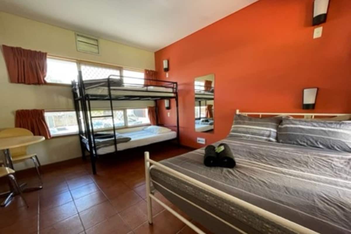 A dormitory room with bunk beds, a desk, and a window.