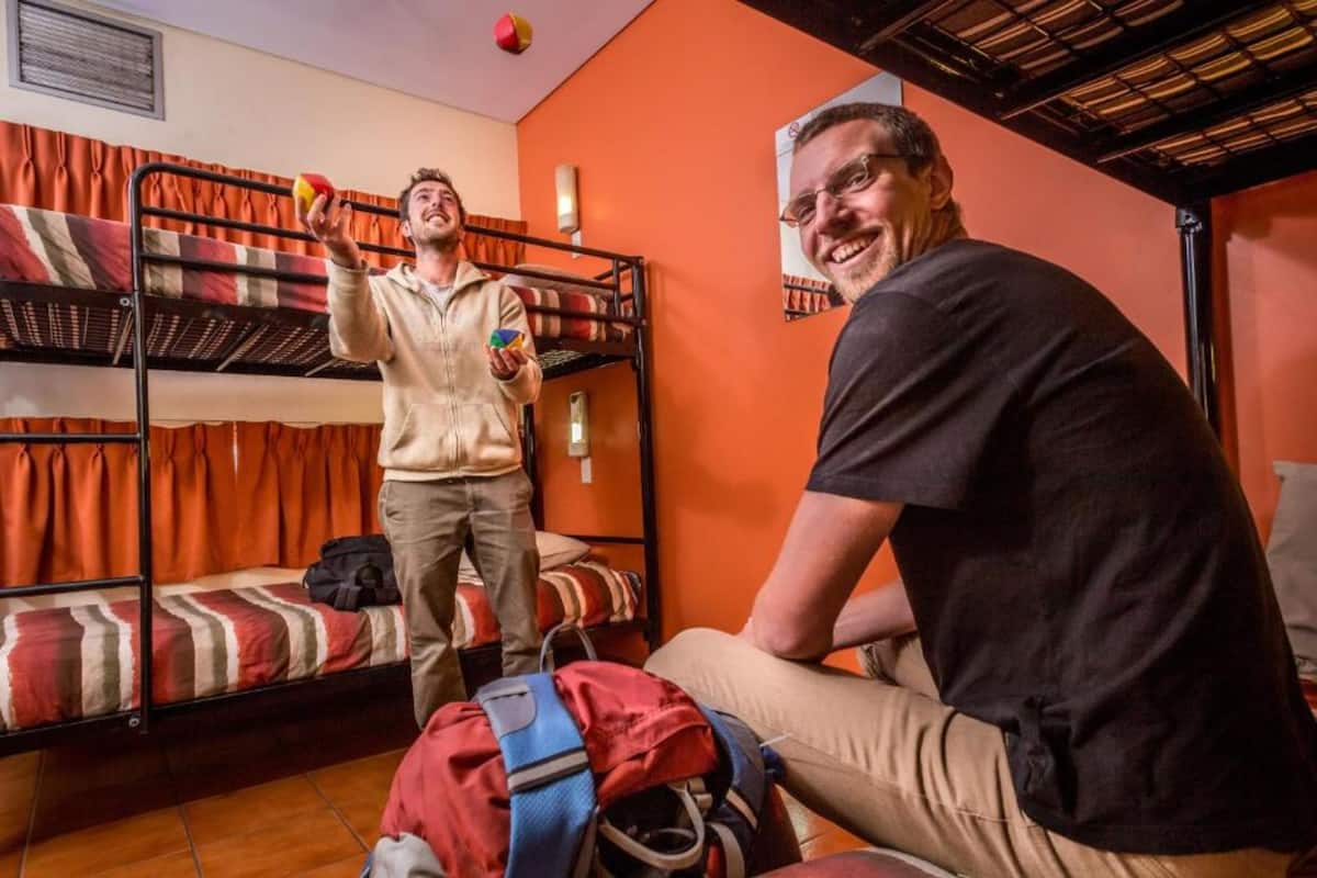 A dormitory room with bunk beds, a red and white striped blanket, and a red backpack on the floor.