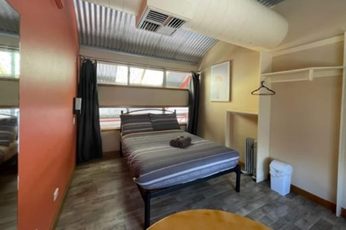 A compact, well-lit room with a single bed, a small table, and a radiator.