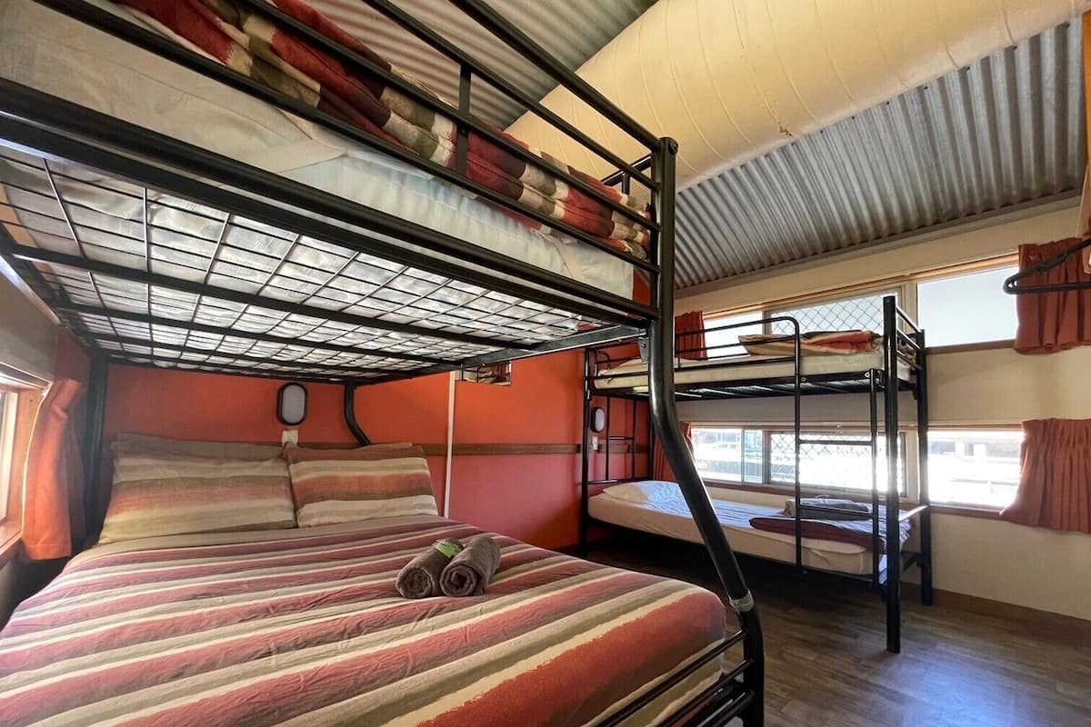 A bunk bed room with a striped bedspread, a window with curtains, and a metal bunk bed structure.