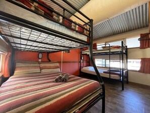 A bunk bed room with a striped bedspread, a window with curtains, and a metal bunk bed structure. - Red Rock Hostel (Alice Springs)