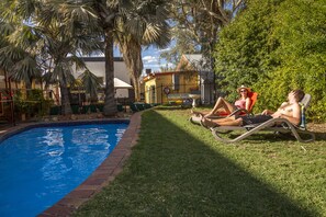 A swimming pool with two sun loungers and a palm tree. - Red Rock Hostel (Alice Springs)
