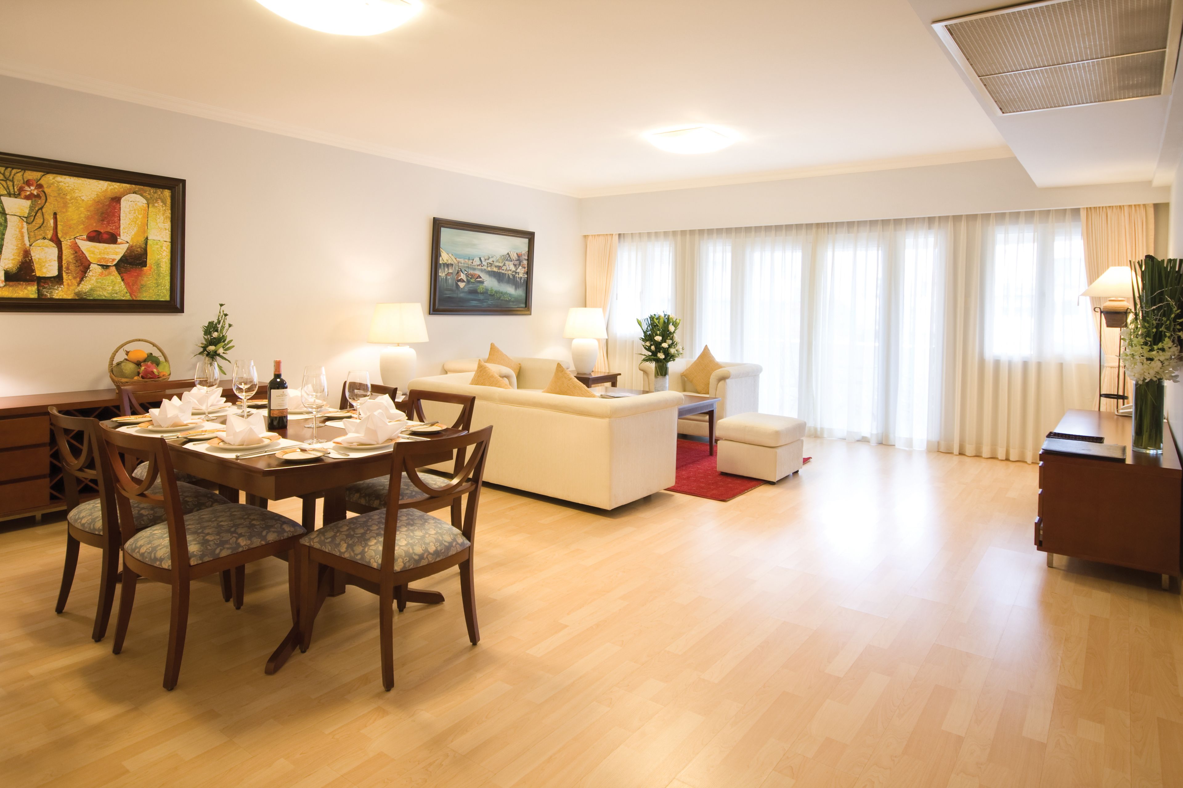 A modern living room with a dining area, featuring a sofa set, a dining table with chairs, and a red rug.