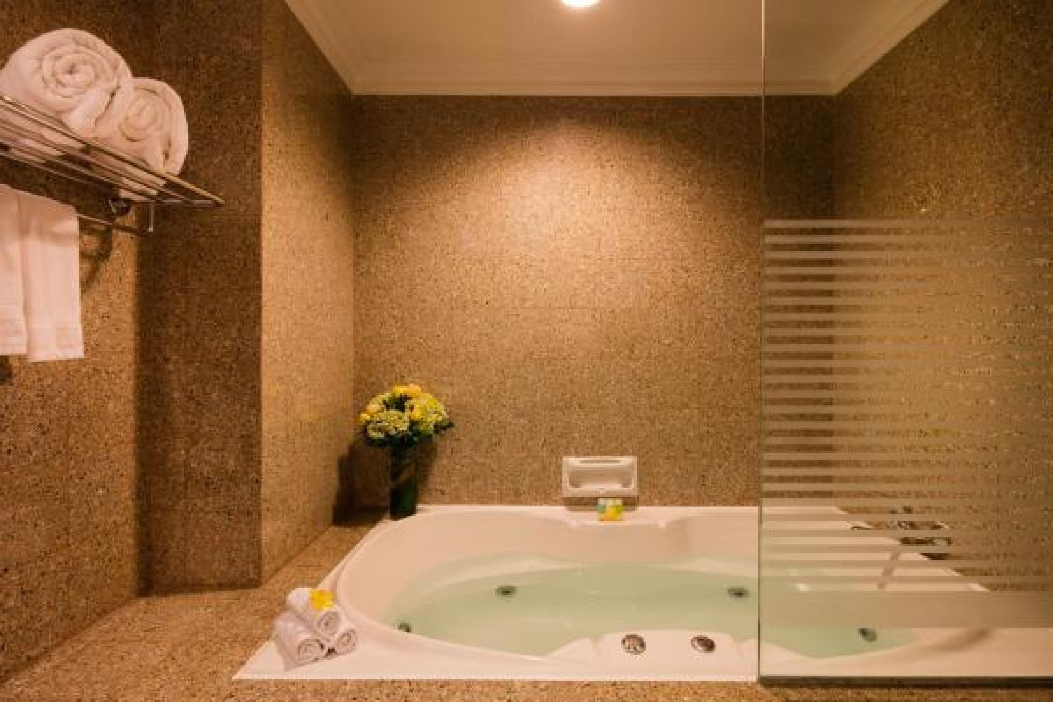 A bathroom with a bathtub, towels, and a vase of flowers.