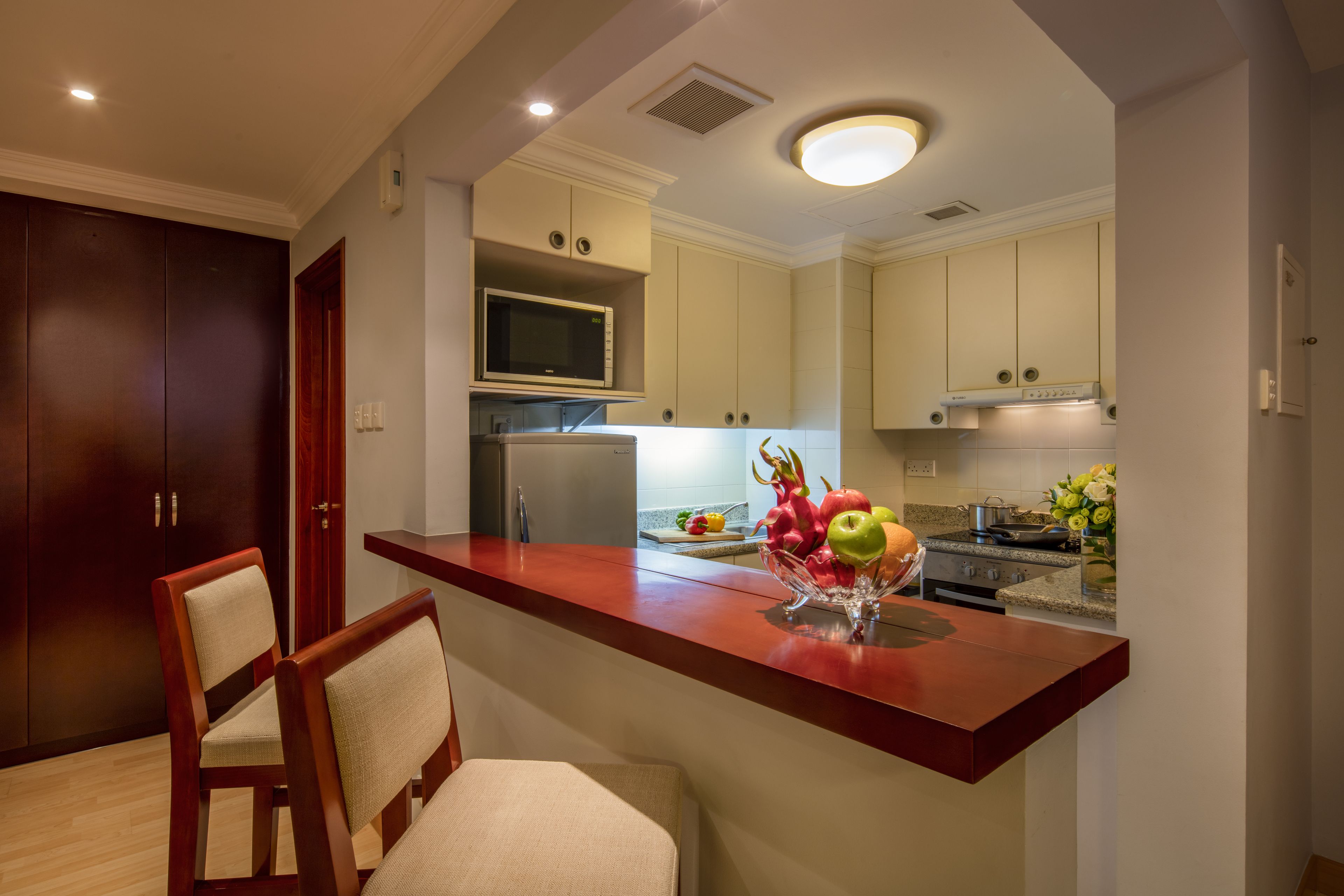 A modern kitchen with a wooden bar counter, a microwave, and a fruit bowl.