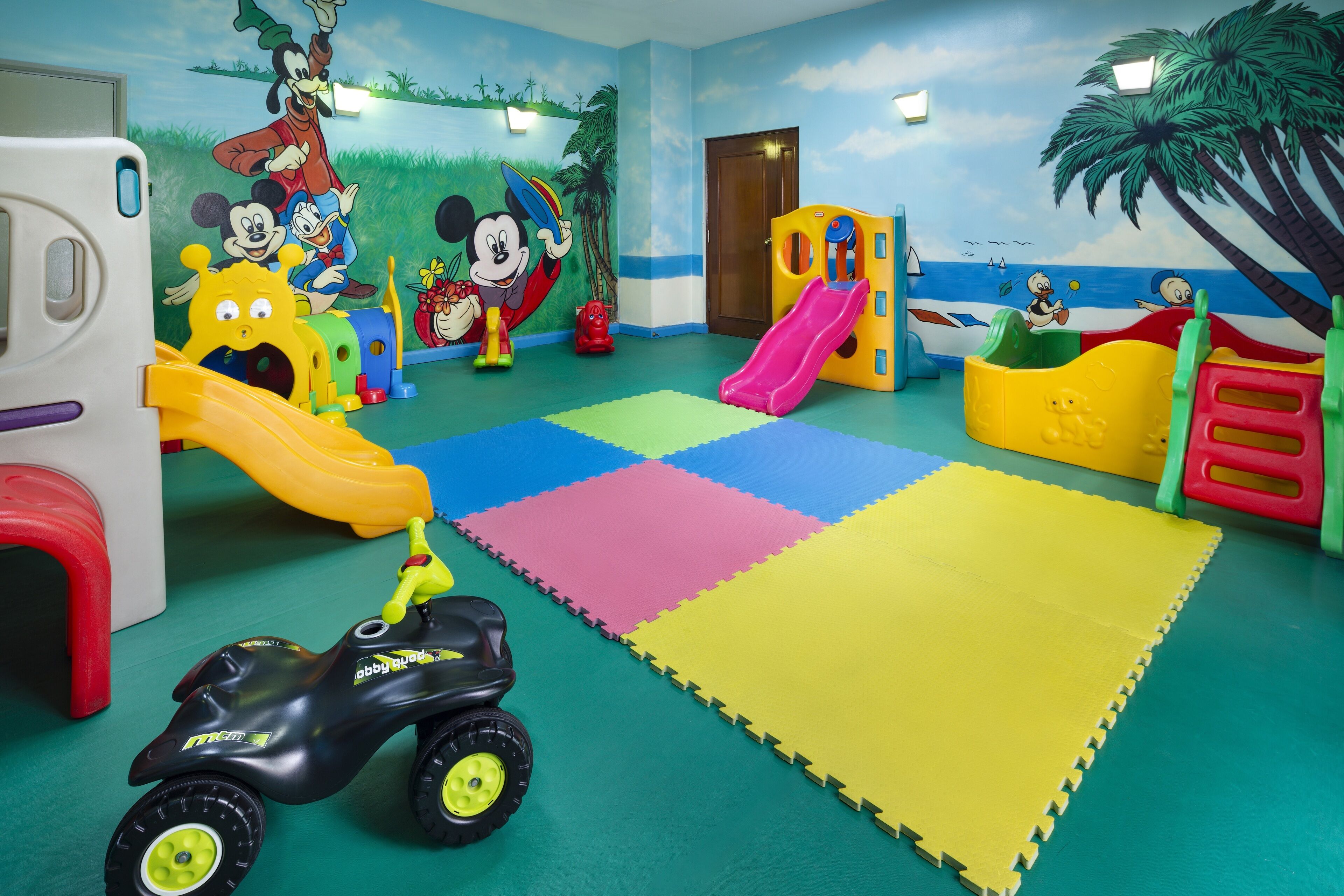 A children's play area with colorful foam mats, a slide, and a toy car.