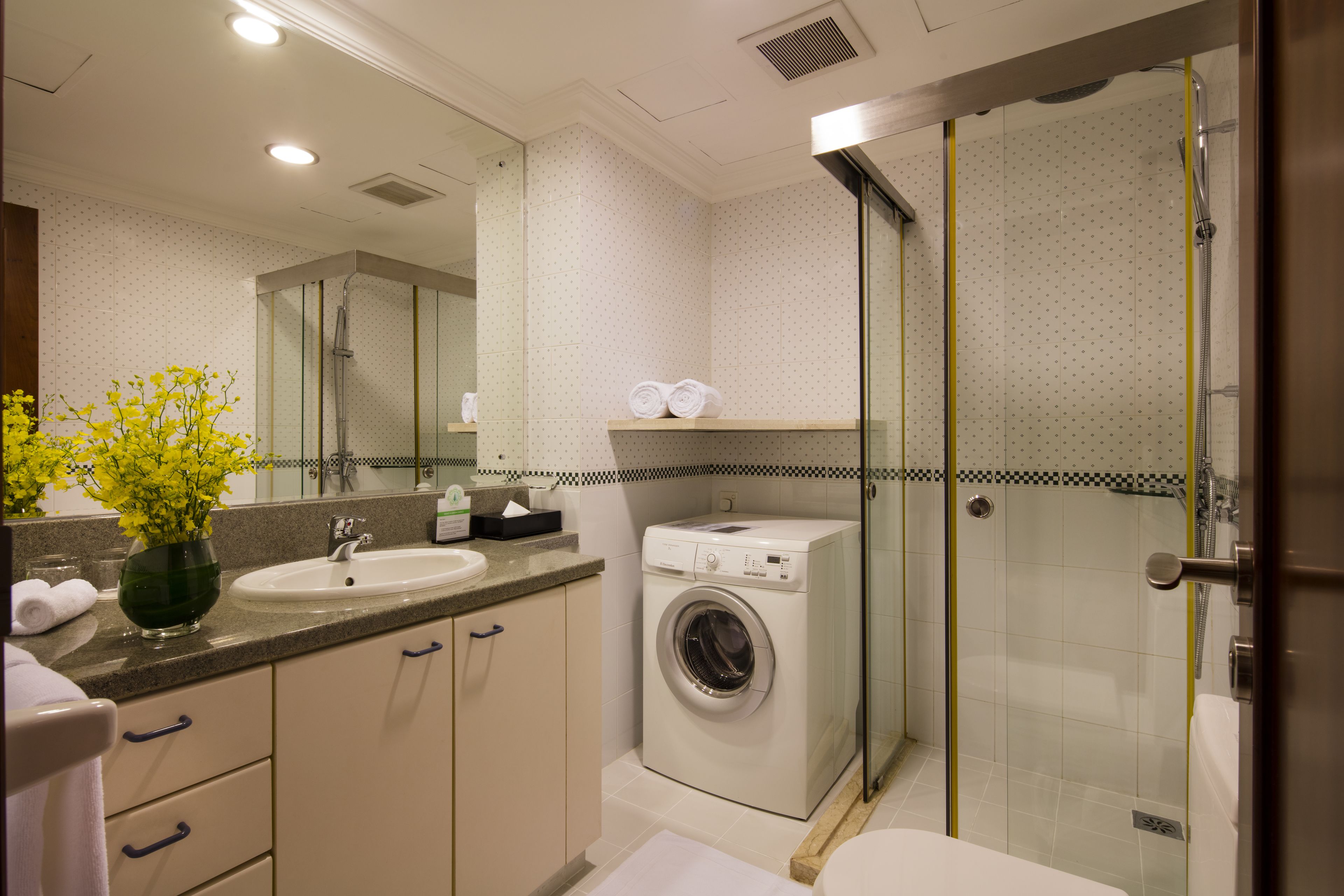 Un baño moderno con lavamanos, espejo, lavadora y ducha con paredes de vidrio.