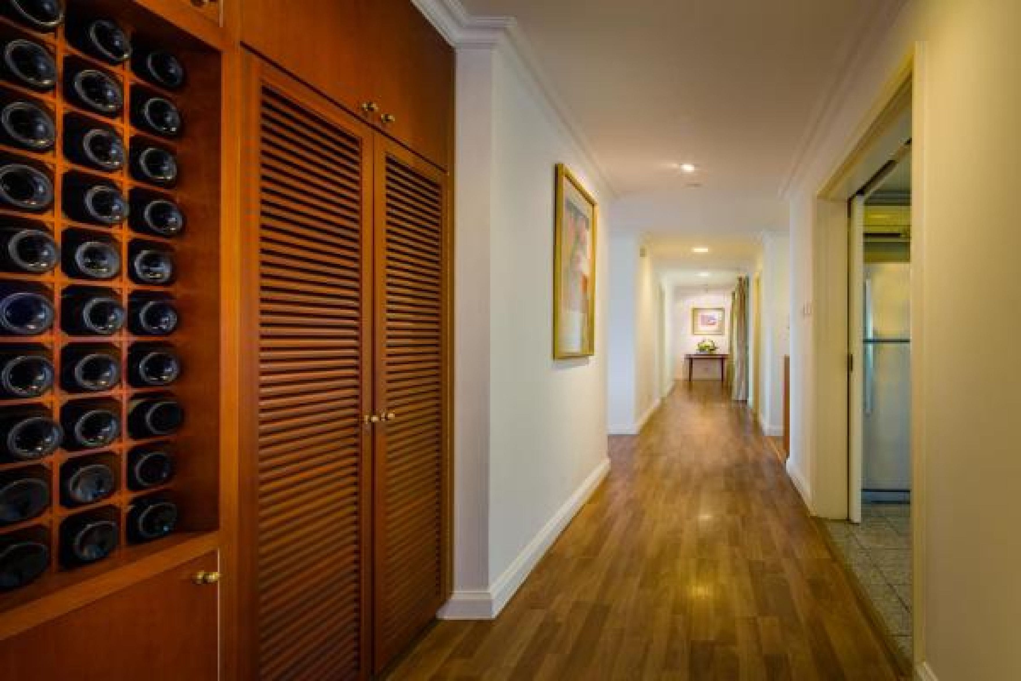 A hallway with wooden flooring and a wine rack on the left.
