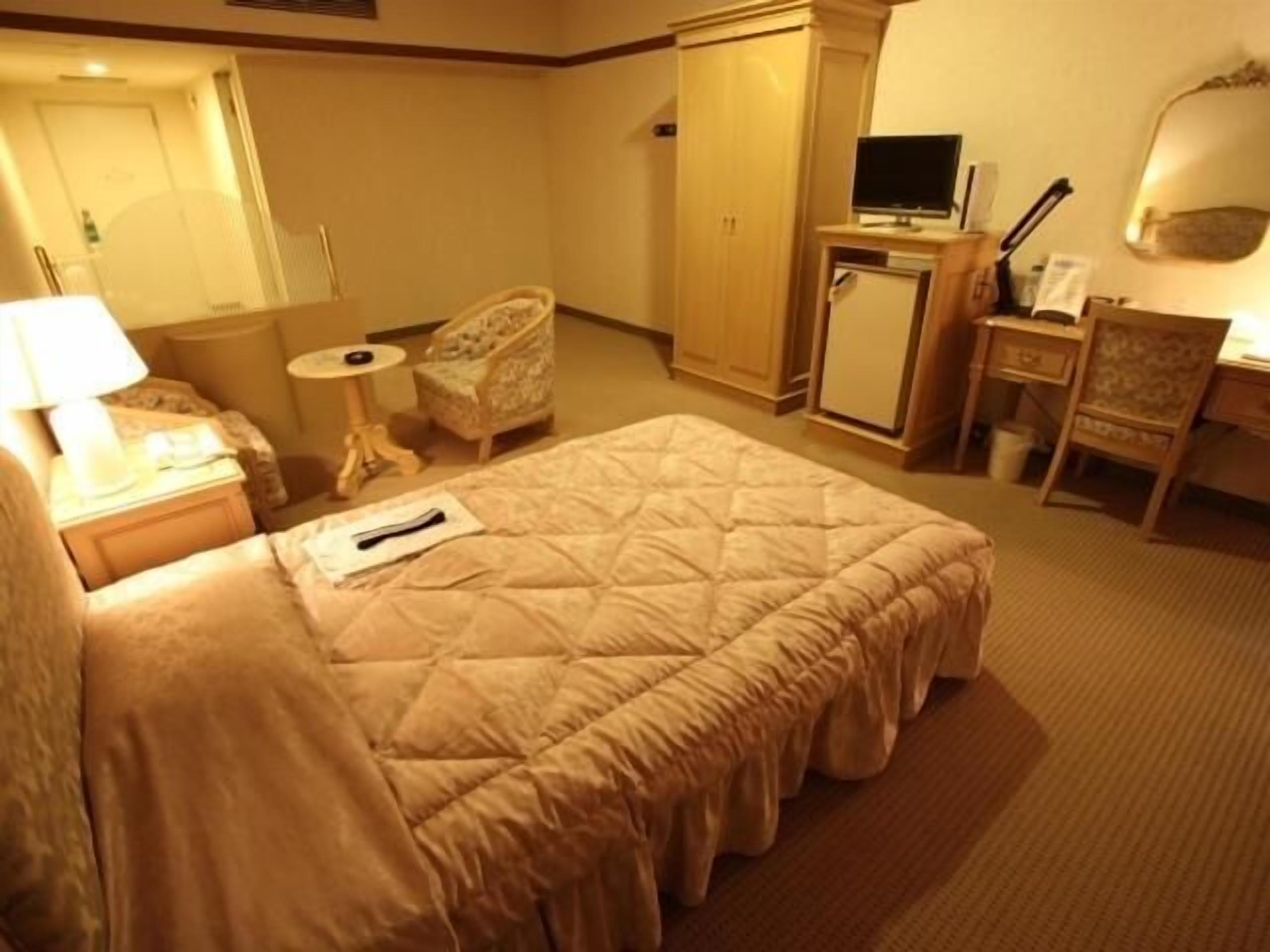A hotel room with a bed, a desk, a chair, a television, and a wardrobe.