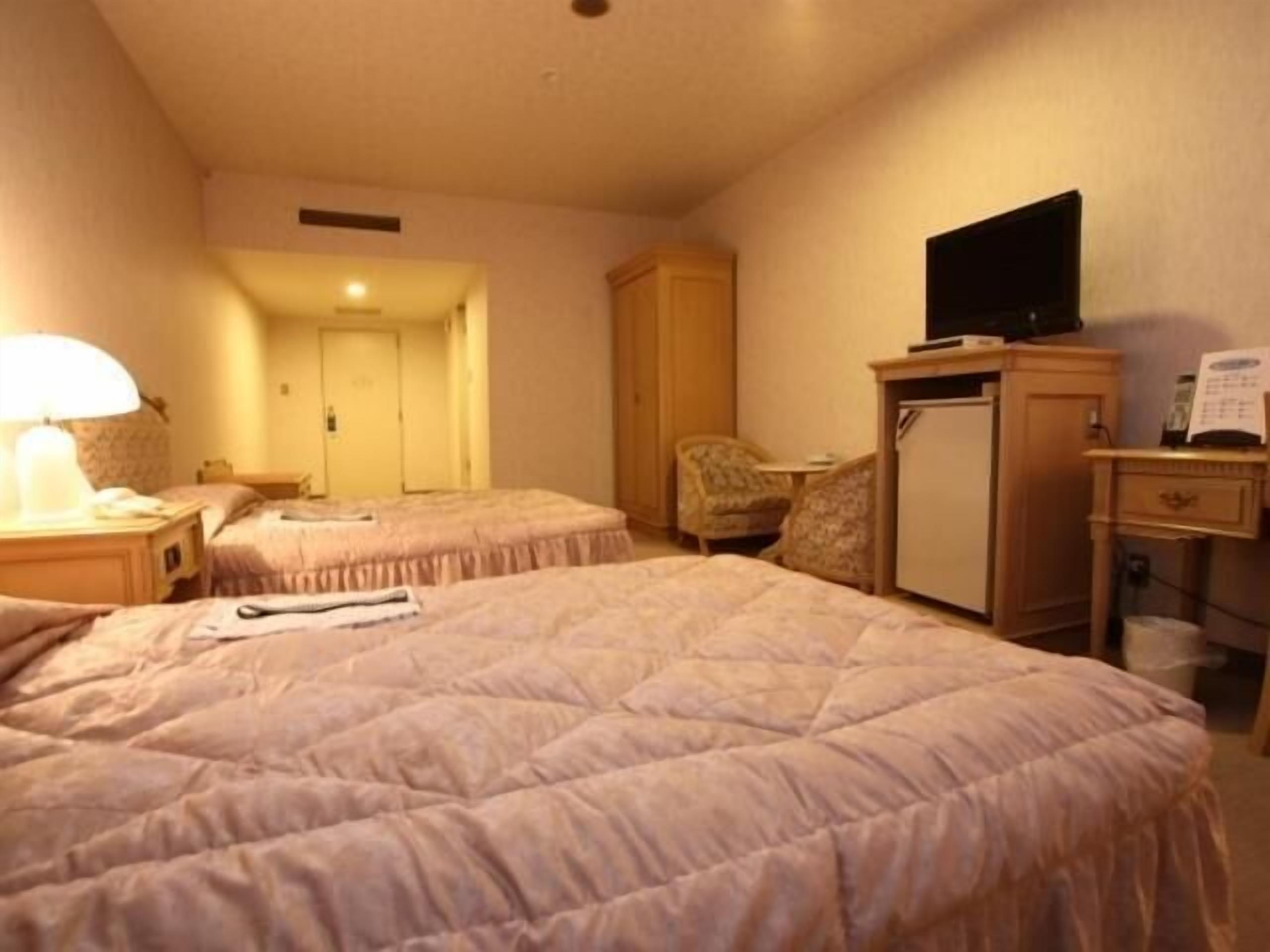 A hotel room with two beds, a television, a desk, and a chair.