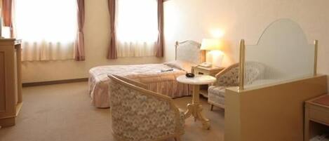 A hotel room with a bed, a chair, a small table, and a mirror.