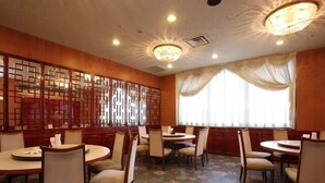 A dining area with round tables and chairs, wooden panel dividers, and a floral carpet. - Nogami President Hotel (Iizuka)