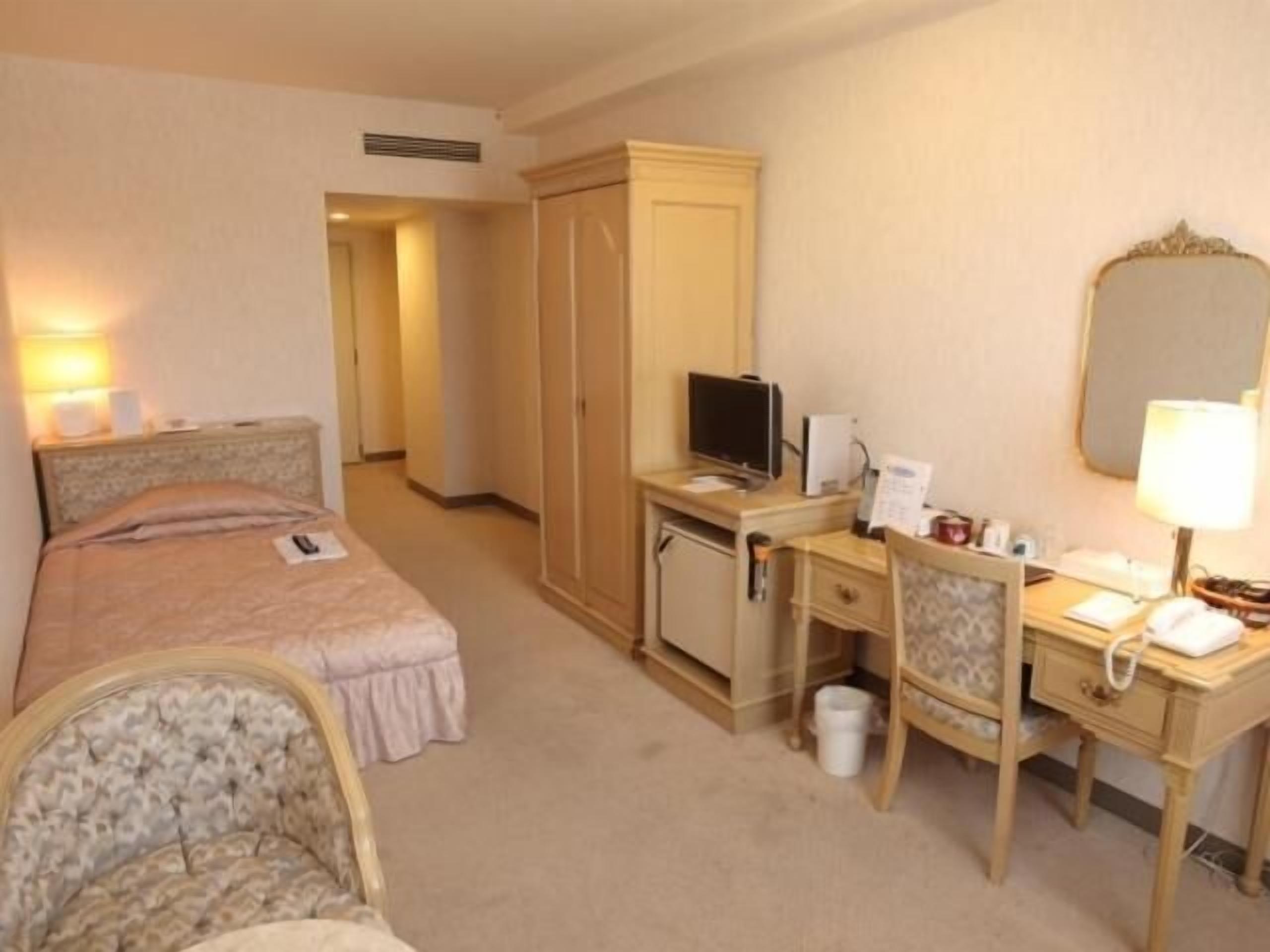 A hotel room with a bed, a desk, a chair, a television, a desk lamp, and a wardrobe.