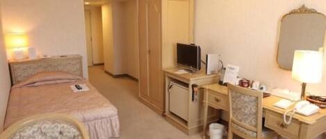 A hotel room with a bed, a desk, a chair, a television, a desk lamp, and a wardrobe.