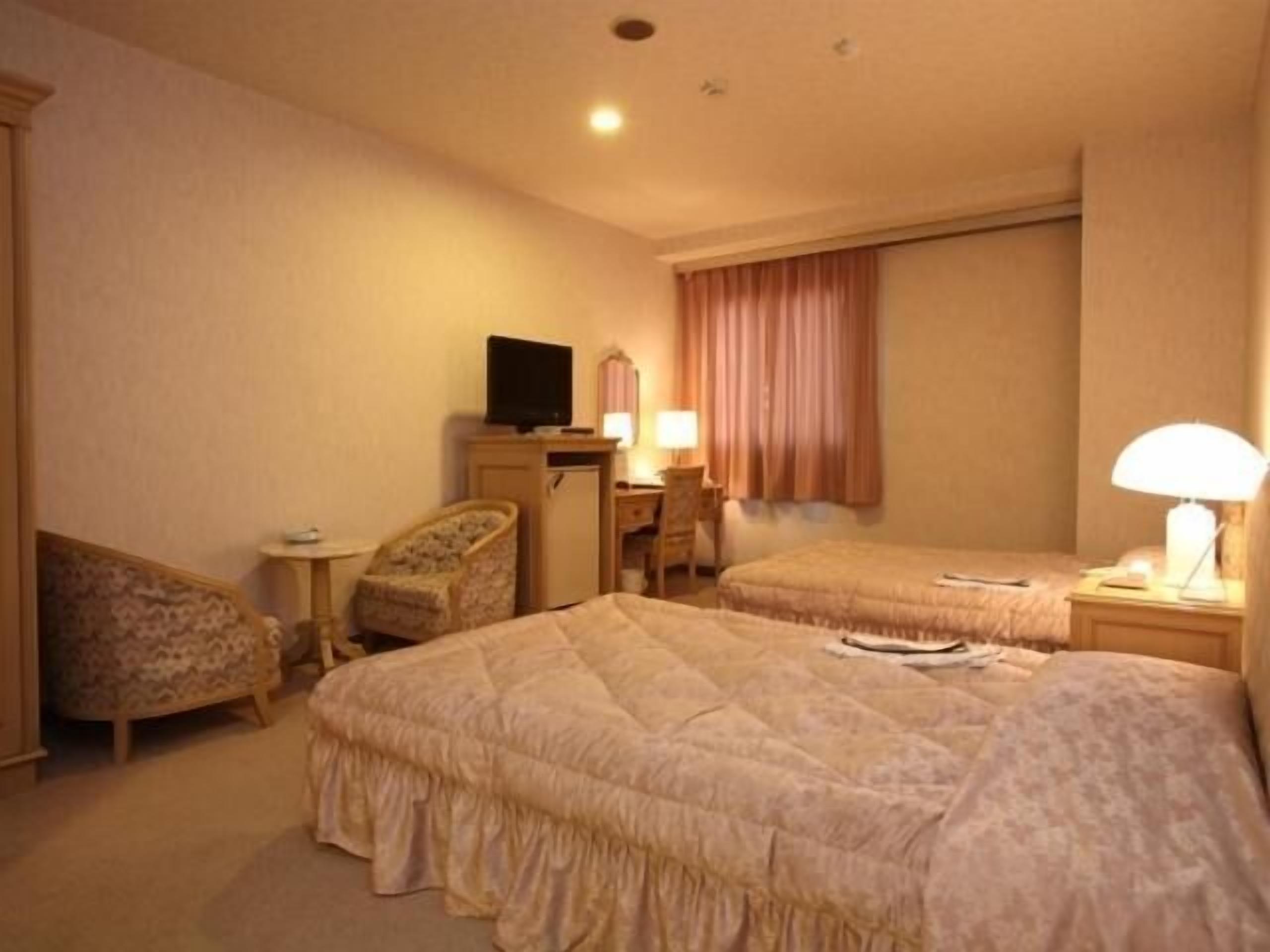 Ein Hotelzimmer mit zwei Betten, einem Schreibtisch, einem Sessel, einem Fernseher und einer Lampe.